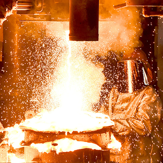 Factory worker wearing protective clothing creating liquid metal. Image is orange with heat and sparks