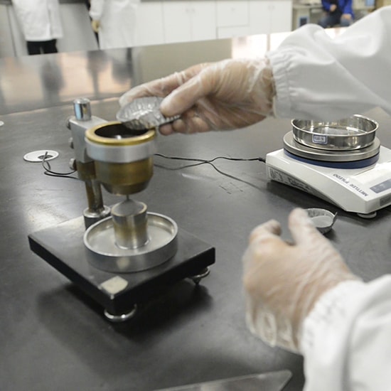 Worker in a white coat and gloves weighing out powder in a lab