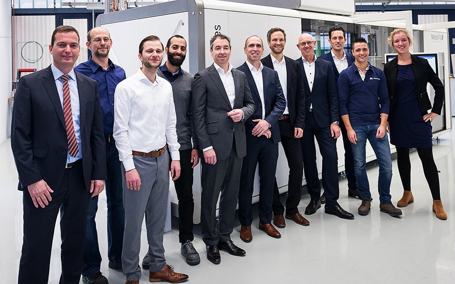 Eleven people standing in front of a large white machine in a factory
